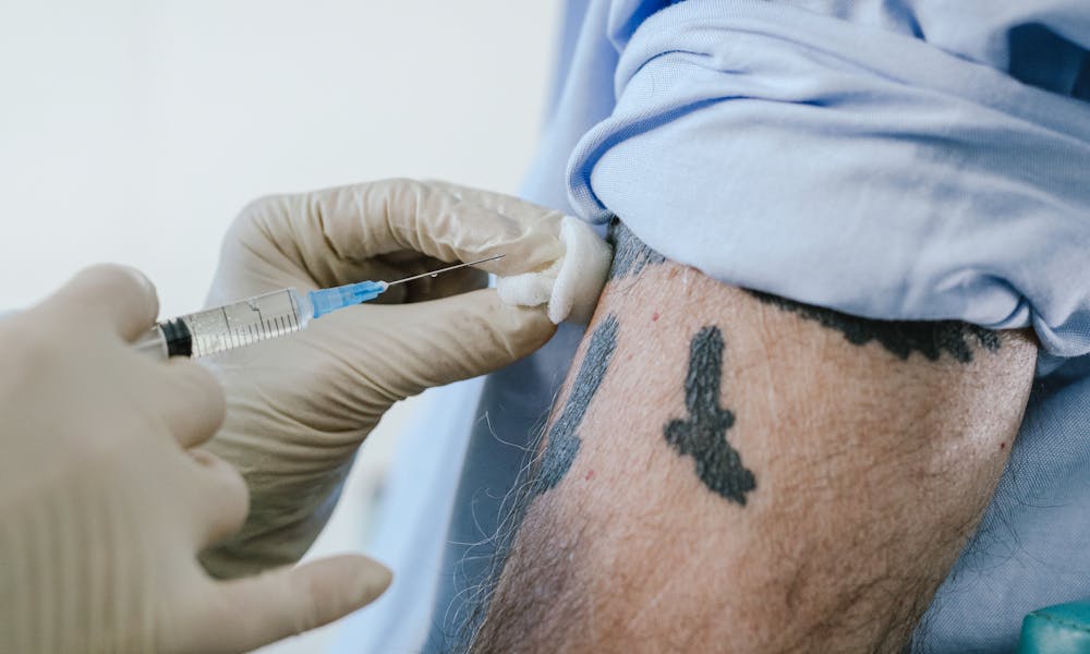 Close-up of a tattooed arm receiving a vaccine injection by a healthcare professional. .pexels