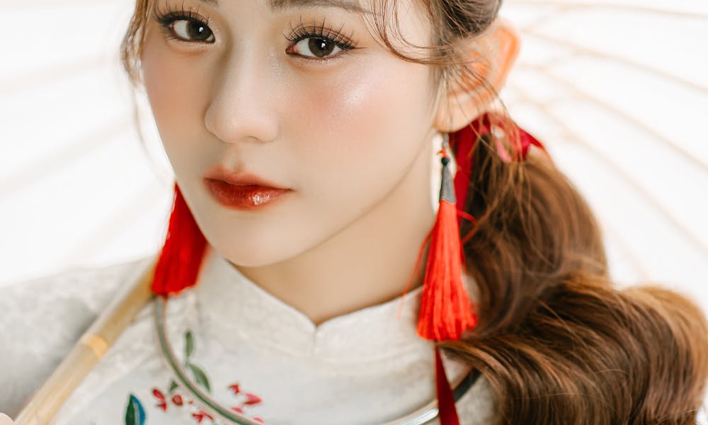 Elegant portrait of a woman in traditional attire with parasol and red tassel earrings. .pexels