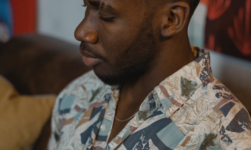 Side view portrait of a thoughtful man with facial hair, sitting indoors in a patterned shirt. .pexels