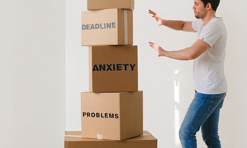 A man in casual attire balances boxes labeled with stress-related words indoors. .pexels