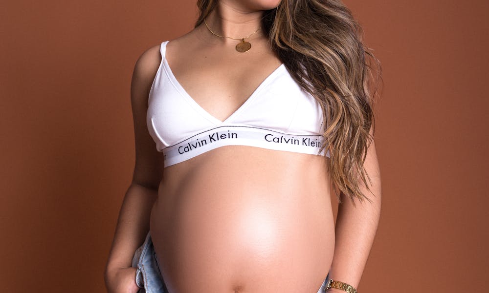 Beautiful smiling pregnant woman in jeans and white top on brown background. .pexels