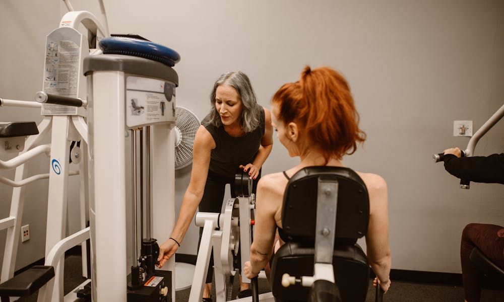A personal trainer guides a woman using gym equipment, promoting healthy living. .pexels