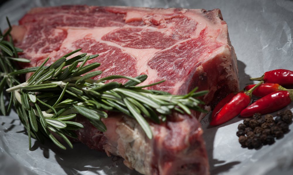 Close-up of a raw steak garnished with rosemary and chilies, ideal for cooking concepts. .pexels
