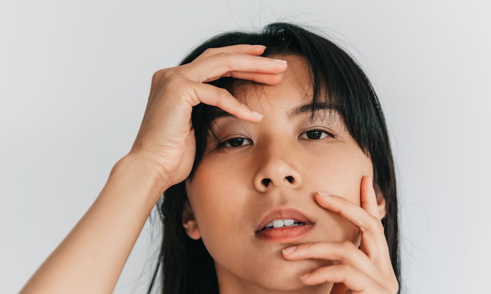 A stunning minimalist portrait of a woman posing with hands on her face in a studio setting. .pexels