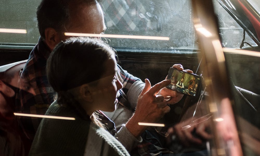 A father and daughter sitting in a car, bonding, watching a smartphone together. .pexels