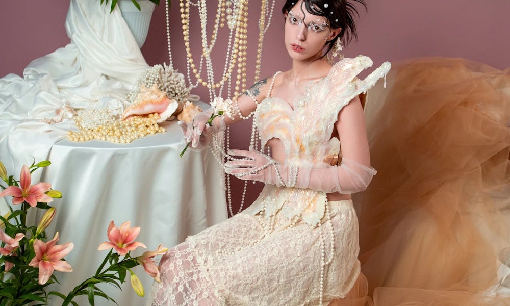 A woman in a vintage dress poses amidst lilies and pearls in an artistic setting. .pexels