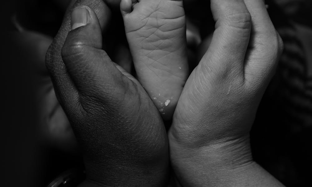 Black and white photo of a baby foot held by parents' hands symbolizing love and care. .pexels