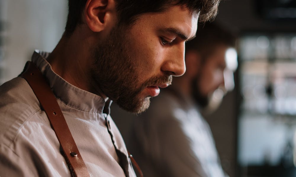A young male chef focused on preparing a dish in a professional kitchen setting. .pexels