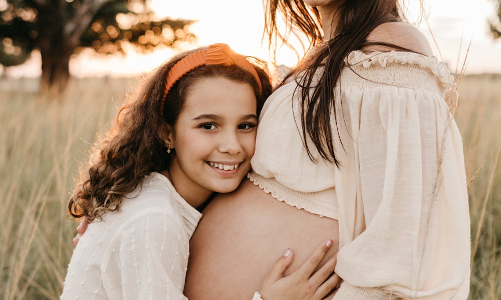 A pregnant woman and her daughter share a joyful moment in a sunlit meadow. .pexels