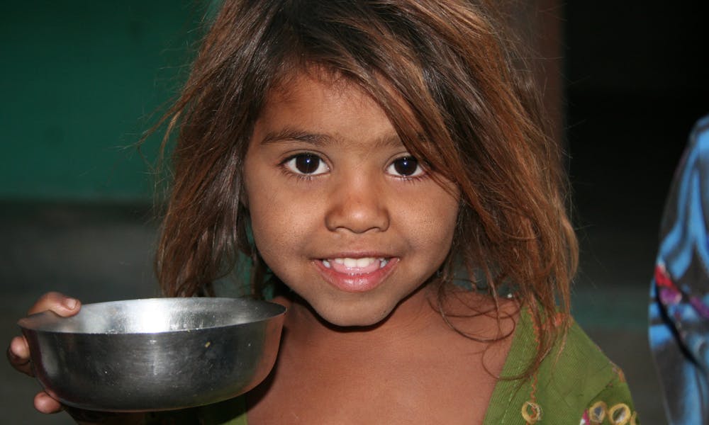 A young girl smiling while holding a metal bowl indoors, reflecting joy and innocence. .pexels