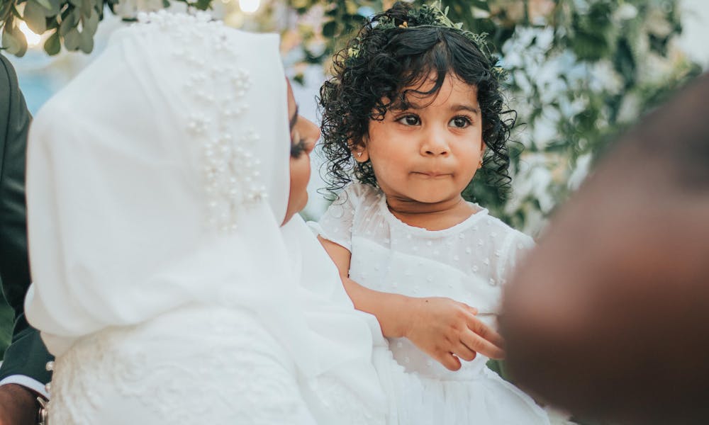 Indian bride in traditional wedding outfit looking at Indian daughter in hands while standing near green plants during holiday celebration .pexels