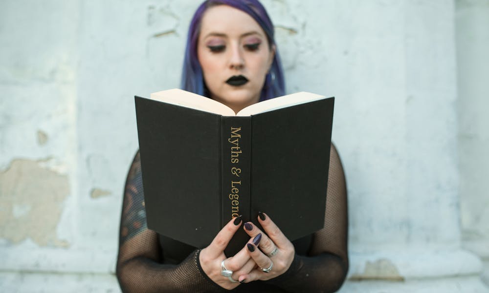 Caucasian woman with gothic style reads 'Myths & Legends' book outside. .pexels