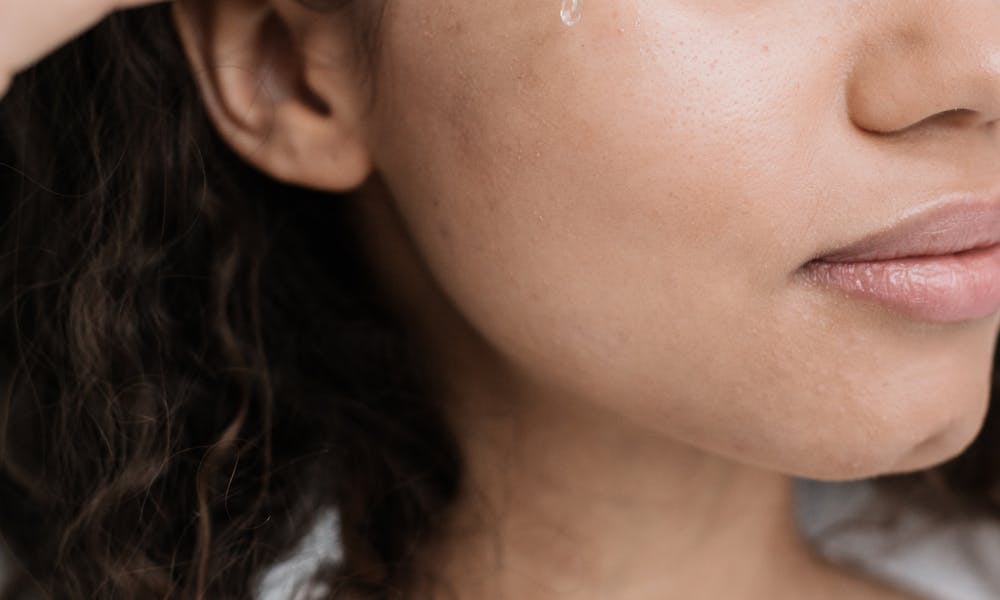 A young woman applying skincare serum to her face with a dropper for a beauty treatment. .pexels